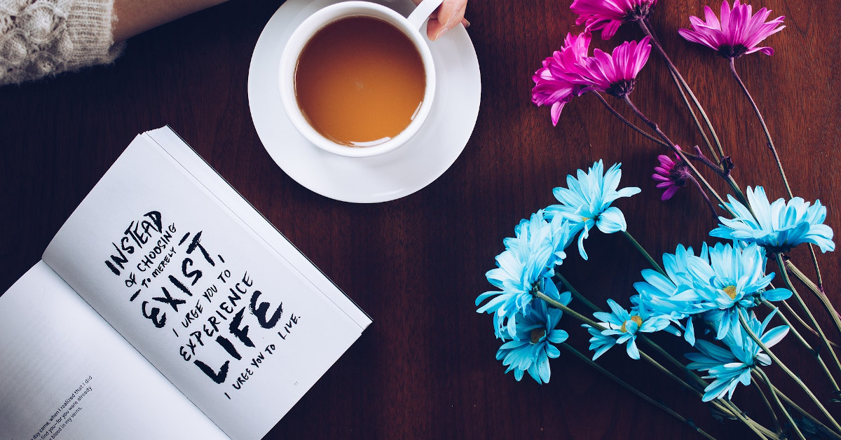 A book, a cup of tea and pink and blue flowers.